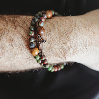 Close-up of a wrist wearing a beaded bracelet with a cross charm on a dark background